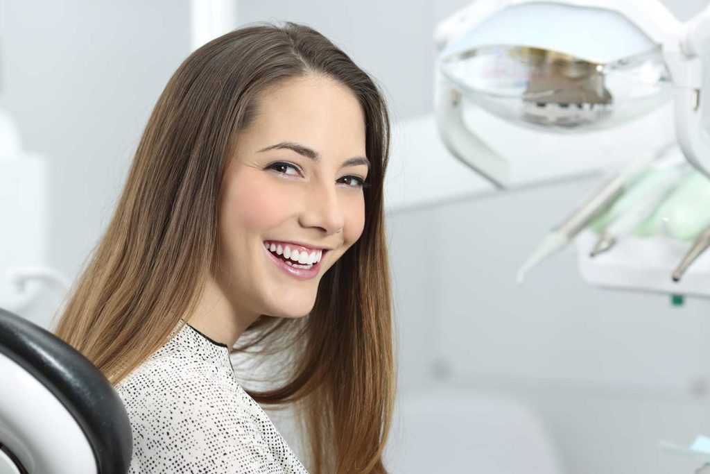 Woman sitting on dentist chair with her head turned back smiling.
