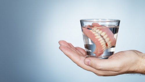 Hand holding glass of water with dentures.