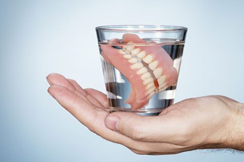 Hand holding glass of water with dentures.