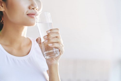 Woman holding slim glass of water.