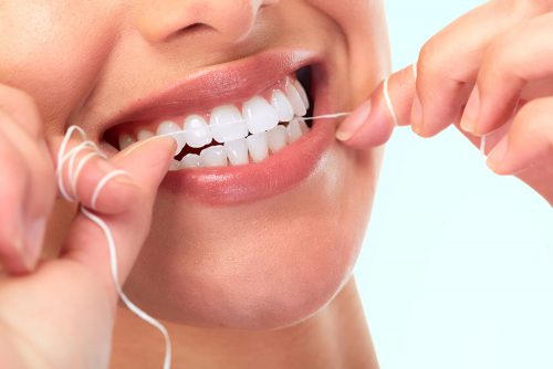 Young woman flosses her healthy teeth.
