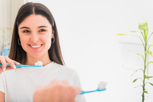 Smiling woman holds toothbrush in front of mirror.