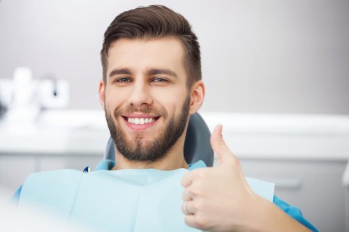 Smiling young man sitting in dental chair giving a thumbs up.