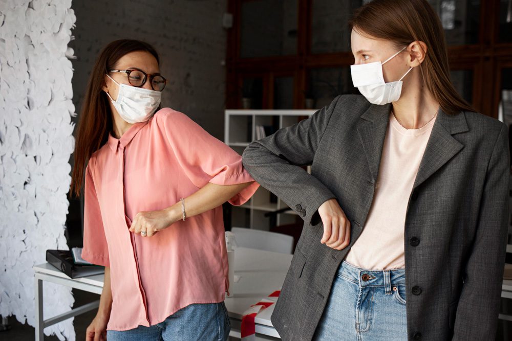 Two women wearing face mask bumping elbows instead of shaking hands to help against the spread of coronavirus.