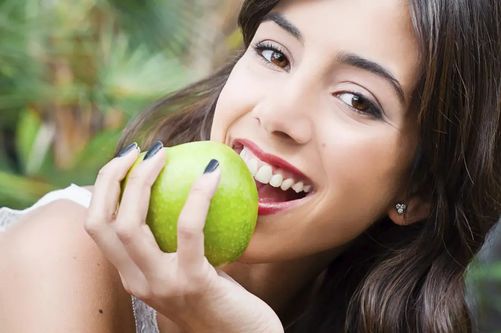 Woman laying down taking bite out of green apple.