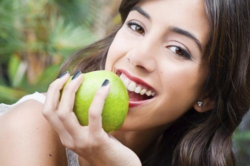 Woman laying down taking bite out of green apple.