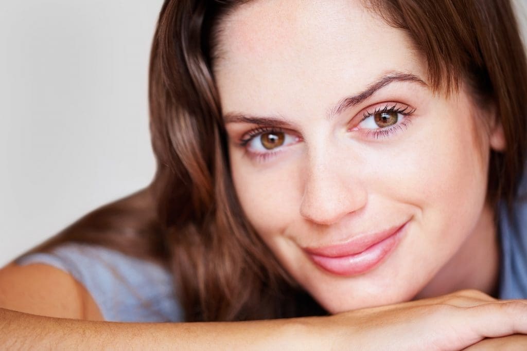 Woman with her head on back of her palm smiling with no teeth.