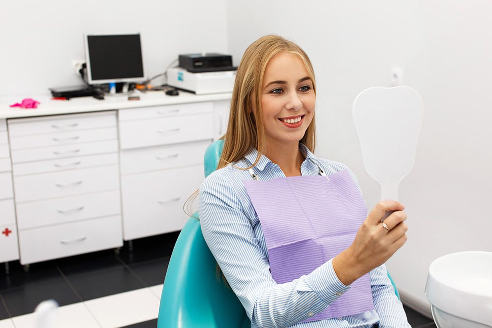 Woman sitting in dentist chair holding mirror to her face