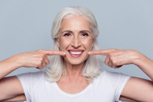 Smiling woman points at her teeth with index fingers.