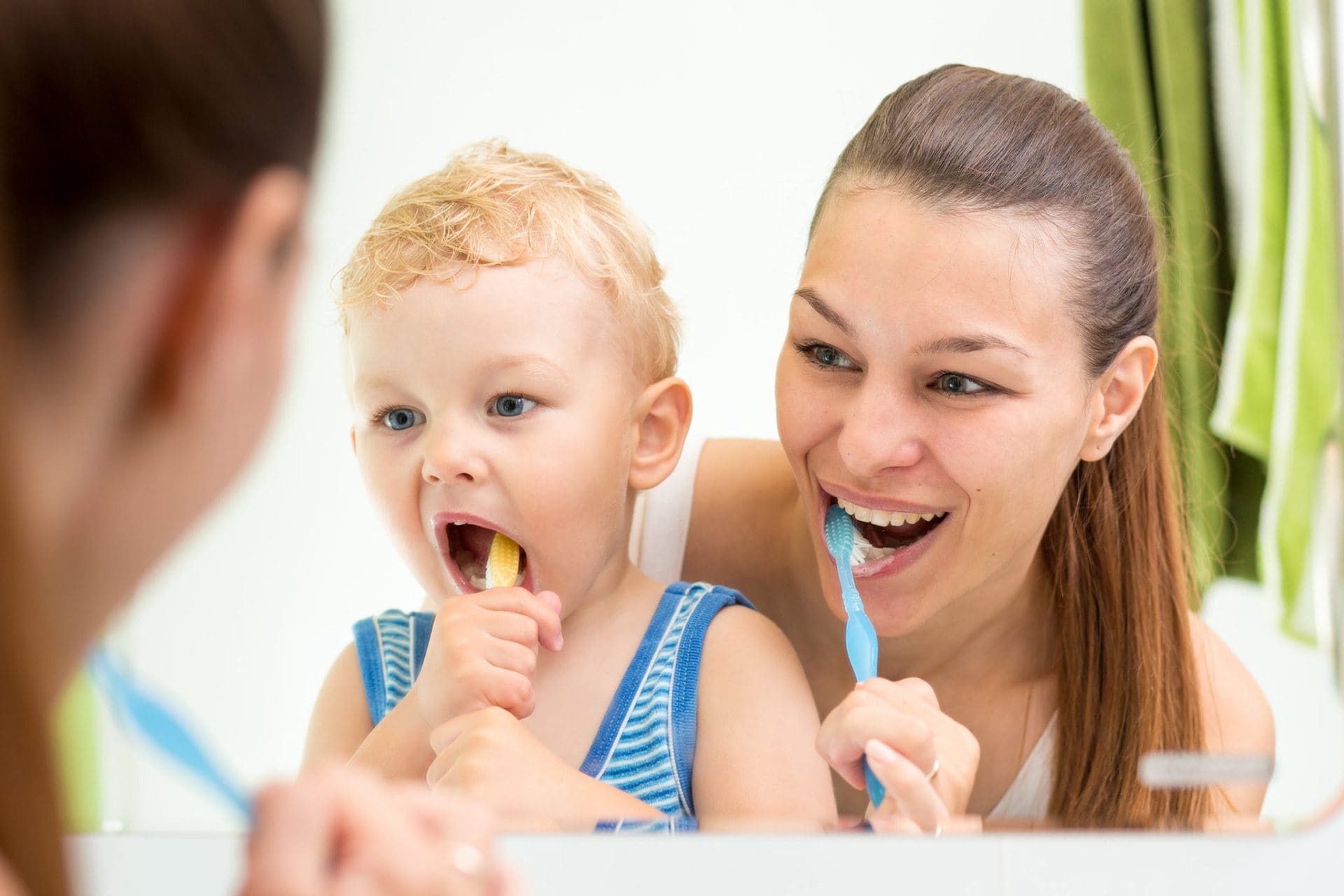 Woman and son brushing their teeth in front of a mirror.
