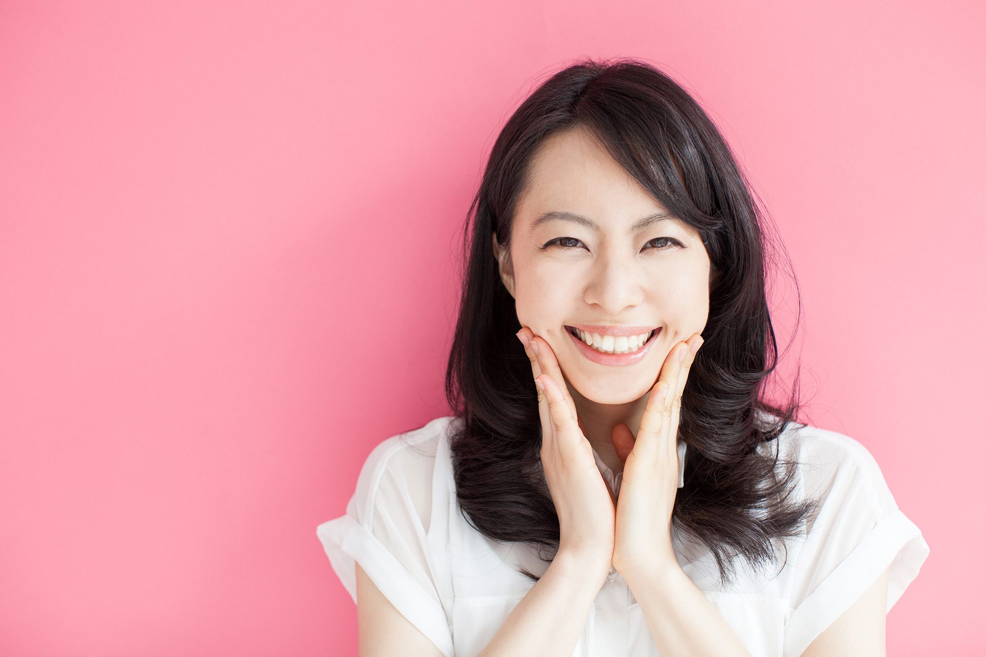 Woman smiling with her hands besides mouth with pink background.