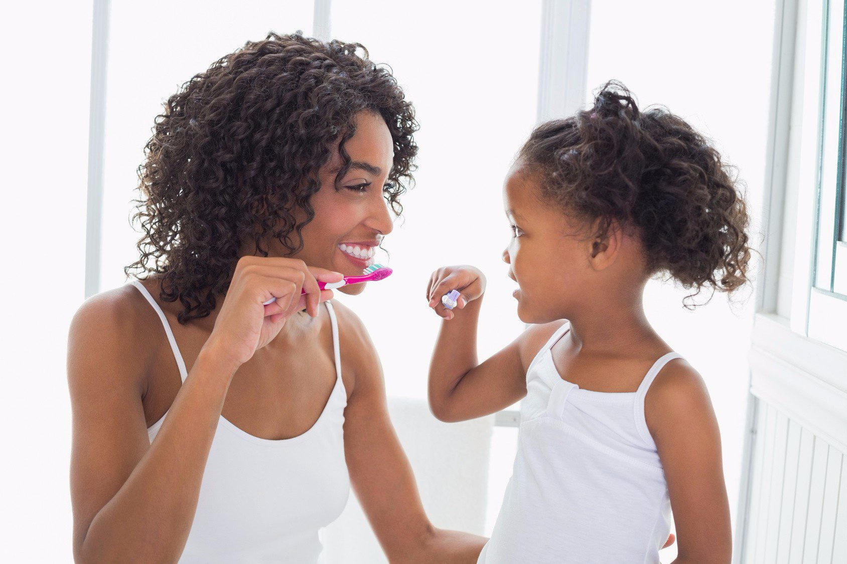 Mother teaching daughter how to brush teeth.