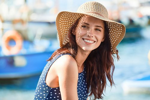 Woman wearing sun hat smiles with blurry boat background.