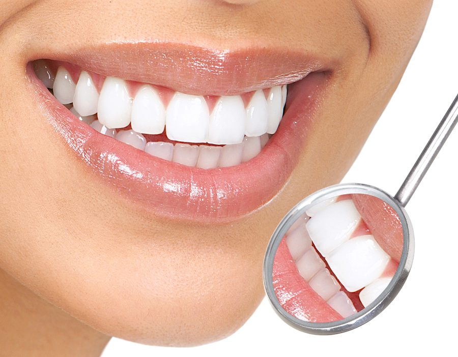 Smiling woman shows healthy teeth with dental mirror in front of mouth.