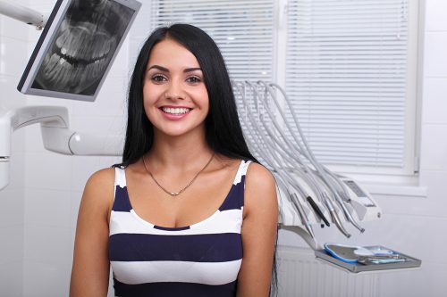 Smiling young woman sits in dentist chair with dental equipment background.