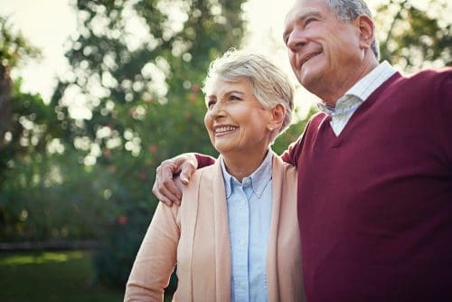 Man giving a side hug to a woman with blurry tree background.