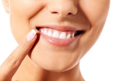 Smiling woman points at her teeth with index finger.