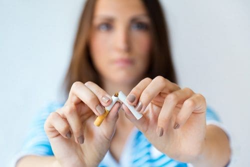 Blurred out woman with arms extended breaking a cigarette in half with her hands.