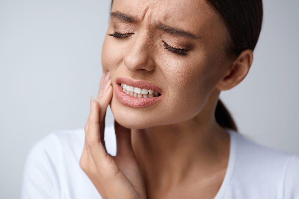Woman holds side of her mouth due to toothache.