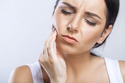 Woman holds side of her mouth due to toothache.