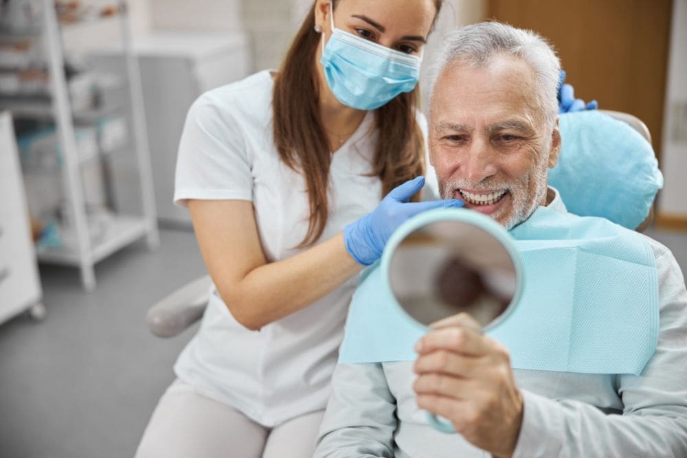 Man Sitting In Dental Chair Looking At Dental Implants With Mirror